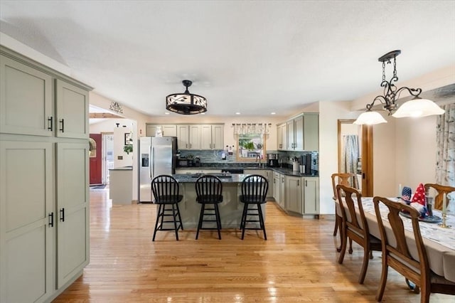 472 Potter Rd, Framingham, MA 01701 - kitchen with stainless steel refrigerator with ice dispenser, dark countertops, a kitchen breakfast bar, light wood-type flooring, and decorative backsplash