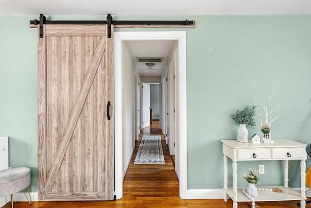 corridor with a barn door, baseboards, visible vents, and wood finished floors