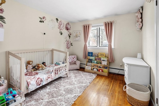 bedroom with a baseboard heating unit, baseboard heating, and hardwood / wood-style flooring