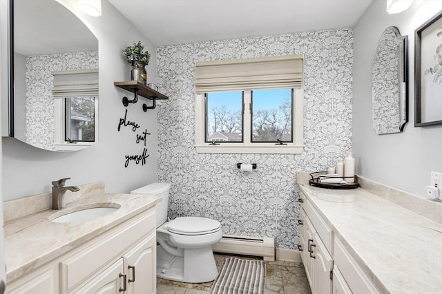 full bath featuring toilet, two vanities, baseboard heating, and a sink