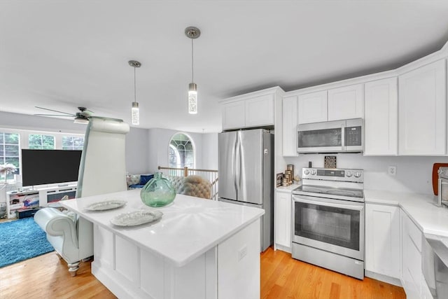 kitchen with appliances with stainless steel finishes, white cabinets, decorative light fixtures, and light hardwood / wood-style flooring