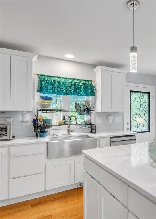 kitchen featuring dishwashing machine, light hardwood / wood-style flooring, sink, white cabinetry, and pendant lighting