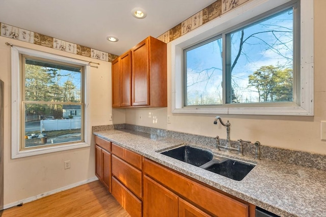 kitchen with light stone countertops, sink, light hardwood / wood-style floors, and stainless steel dishwasher