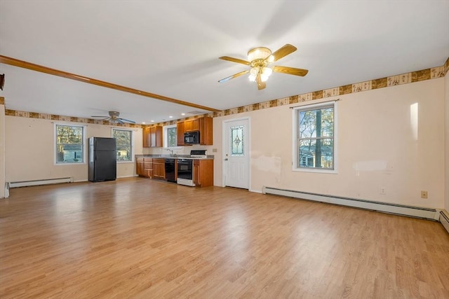 unfurnished living room featuring a wealth of natural light, light wood-type flooring, and a baseboard heating unit