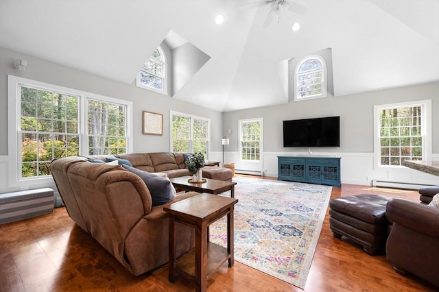living room featuring baseboard heating, high vaulted ceiling, a wainscoted wall, and plenty of natural light