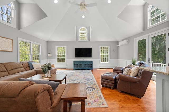 living room featuring a ceiling fan, baseboard heating, an AC wall unit, high vaulted ceiling, and a wainscoted wall