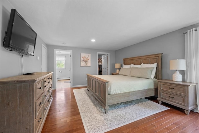 bedroom featuring wood finished floors, a walk in closet, baseboards, a baseboard radiator, and recessed lighting