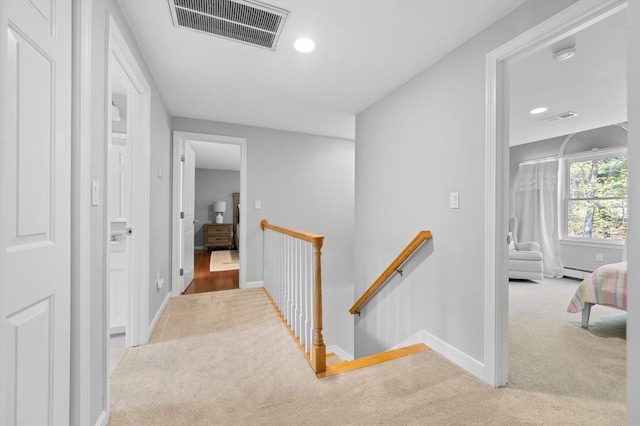 corridor with visible vents, an upstairs landing, a baseboard radiator, and carpet floors