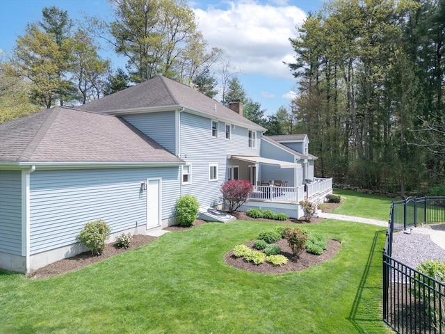 rear view of property featuring a yard, a chimney, a wooden deck, and roof with shingles