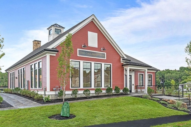 view of front facade with a chimney, a front lawn, and fence