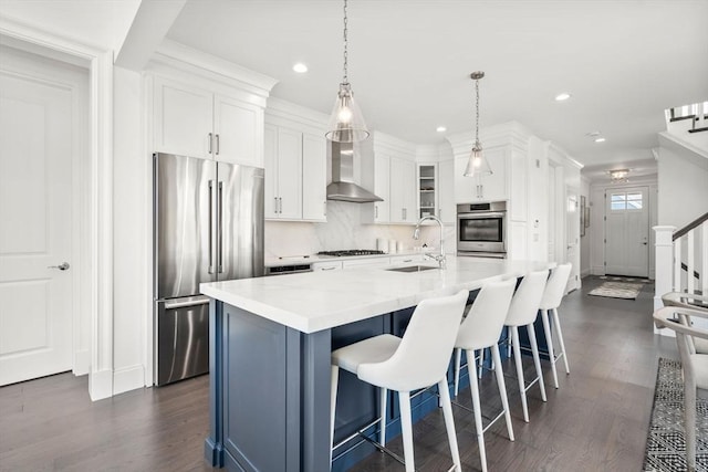kitchen featuring a sink, wall chimney range hood, dark wood-style flooring, white cabinets, and appliances with stainless steel finishes