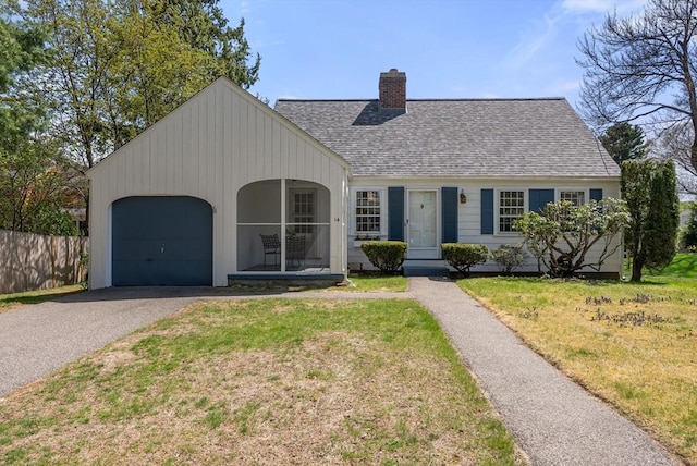 view of front facade with roof with shingles, an attached garage, aphalt driveway, a front yard, and a chimney