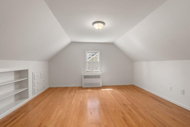 additional living space with light wood-style floors, baseboards, built in features, and radiator heating unit