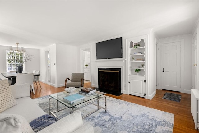 living room with baseboards, a fireplace with flush hearth, wood finished floors, and an inviting chandelier