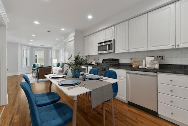 kitchen featuring hardwood / wood-style floors, decorative backsplash, white cabinetry, and appliances with stainless steel finishes