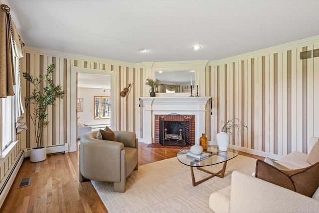 living room with ornamental molding, wood finished floors, a fireplace, wallpapered walls, and a baseboard heating unit