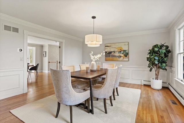 dining room with visible vents, crown molding, wainscoting, a baseboard radiator, and light wood-style flooring