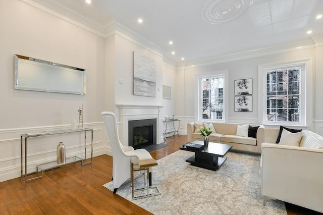 living area with a fireplace with flush hearth, wood finished floors, a decorative wall, wainscoting, and crown molding