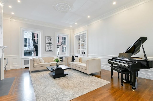 living area with ornamental molding, built in features, wood finished floors, wainscoting, and a decorative wall