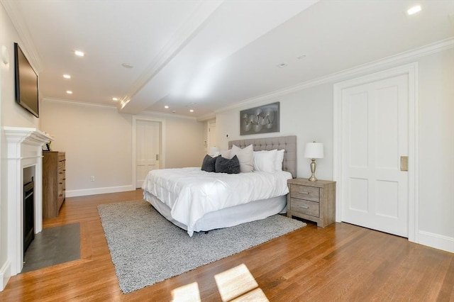bedroom featuring a fireplace with flush hearth, baseboards, crown molding, and light wood-style floors