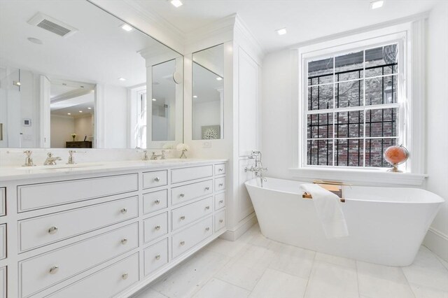 bathroom with a freestanding bath, double vanity, visible vents, and a sink