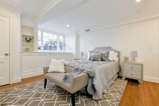 bedroom featuring baseboards, wood finished floors, visible vents, and ornamental molding