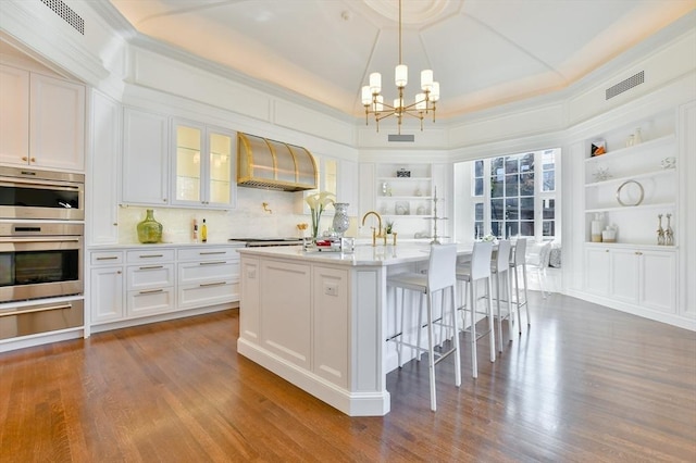 kitchen featuring built in shelves, wall chimney range hood, a chandelier, appliances with stainless steel finishes, and a warming drawer