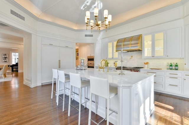 kitchen with visible vents, white cabinetry, wall chimney exhaust hood, and an inviting chandelier