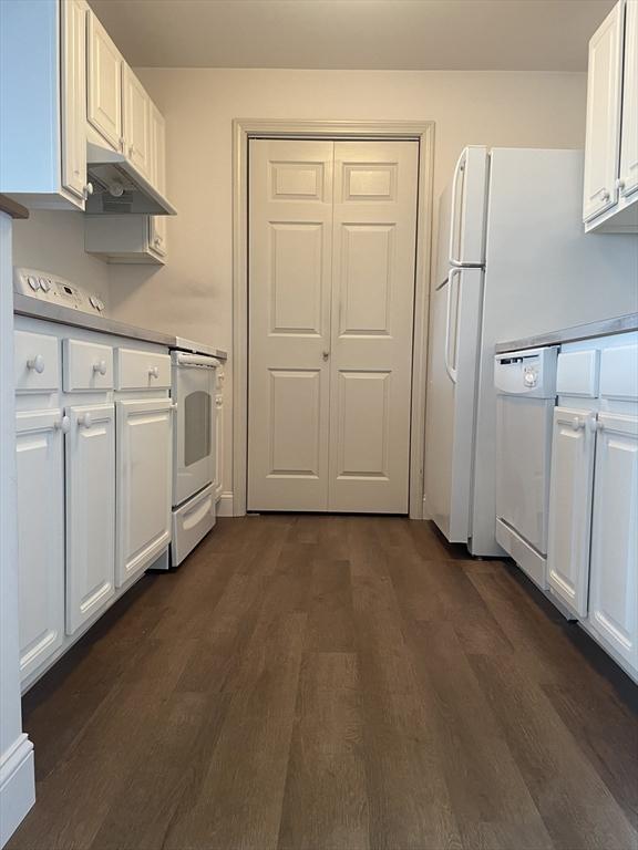 kitchen with white appliances, dark hardwood / wood-style floors, and white cabinets