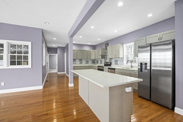 kitchen featuring decorative backsplash, wall chimney exhaust hood, stainless steel appliances, light countertops, and a sink