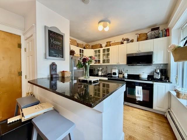19 S St Unit 11, Boston, MA 02135 - kitchen featuring a baseboard radiator, appliances with stainless steel finishes, glass insert cabinets, dark stone counters, and a kitchen bar