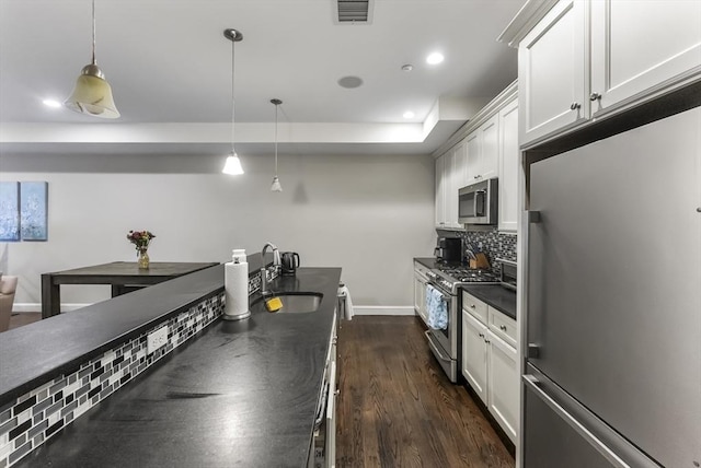 kitchen with stainless steel appliances, a sink, dark countertops, dark wood-style flooring, and backsplash