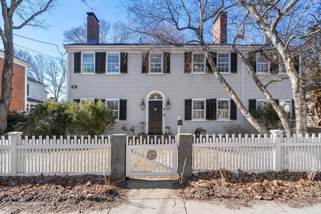 colonial inspired home featuring a chimney and a fenced front yard