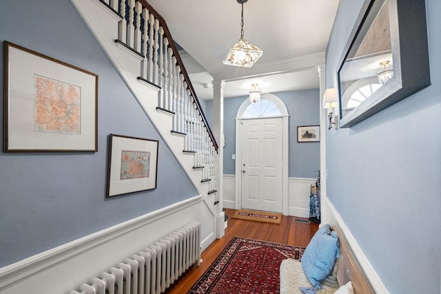 entrance foyer with wainscoting, radiator heating unit, wood finished floors, stairs, and ornate columns