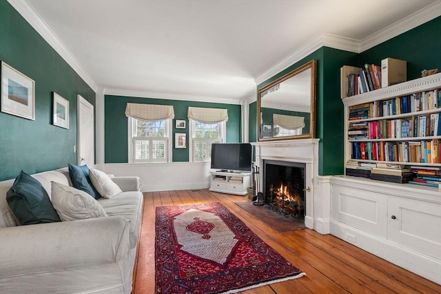 living room with a warm lit fireplace, wood-type flooring, and crown molding