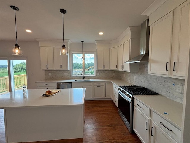 kitchen with appliances with stainless steel finishes, sink, wall chimney range hood, pendant lighting, and white cabinets