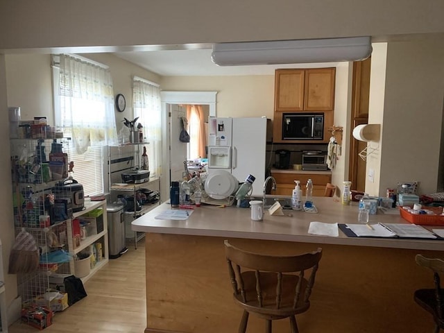 kitchen featuring kitchen peninsula, light wood-type flooring, black microwave, and white fridge with ice dispenser