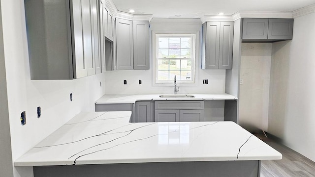 kitchen with light stone counters, ornamental molding, gray cabinets, and a sink