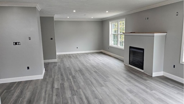 unfurnished living room featuring baseboards, a glass covered fireplace, light wood-style flooring, and crown molding