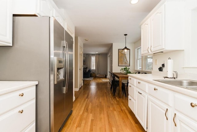 kitchen with white cabinets, light hardwood / wood-style flooring, a wealth of natural light, stainless steel fridge, and pendant lighting