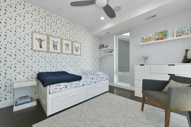 bedroom featuring visible vents, an accent wall, ceiling fan, baseboards, and wallpapered walls