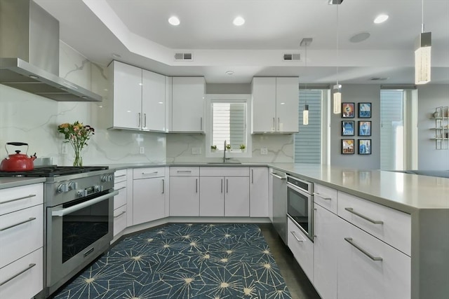 kitchen with a peninsula, a sink, visible vents, appliances with stainless steel finishes, and wall chimney exhaust hood