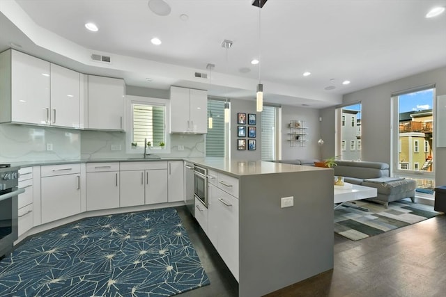 kitchen with visible vents, open floor plan, a peninsula, white cabinetry, and a sink