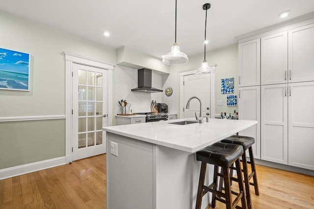 kitchen featuring wall chimney exhaust hood, a sink, light wood-style floors, stainless steel electric stove, and light stone counters