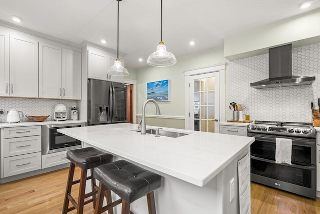 kitchen featuring wall chimney range hood, appliances with stainless steel finishes, a sink, decorative backsplash, and recessed lighting