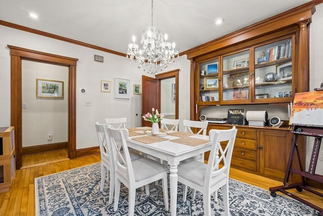 dining space with light wood-style floors, a chandelier, crown molding, and baseboards