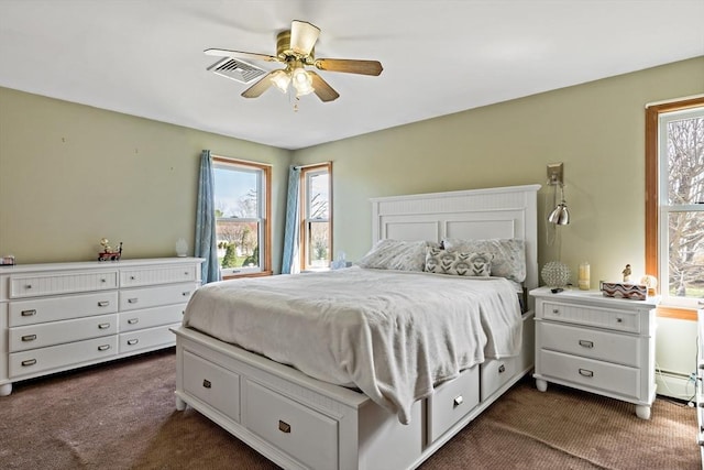 bedroom featuring a ceiling fan, visible vents, dark carpet, and multiple windows