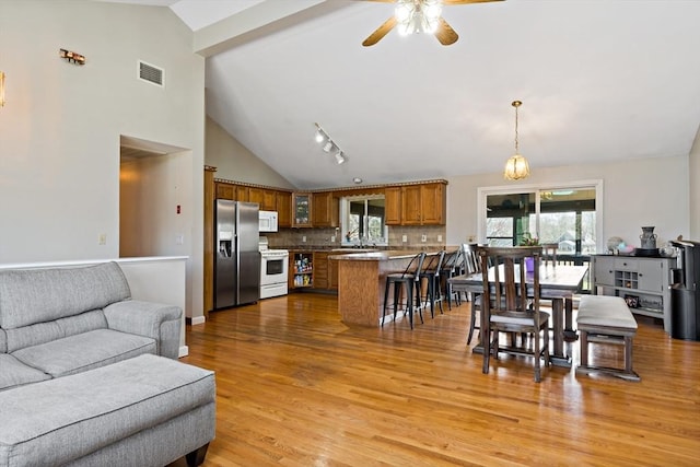 living room featuring light wood finished floors, visible vents, ceiling fan, and high vaulted ceiling