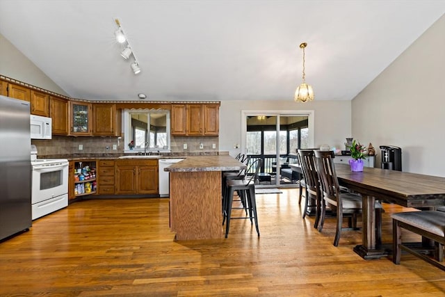 kitchen featuring vaulted ceiling, white appliances, a kitchen bar, and brown cabinets