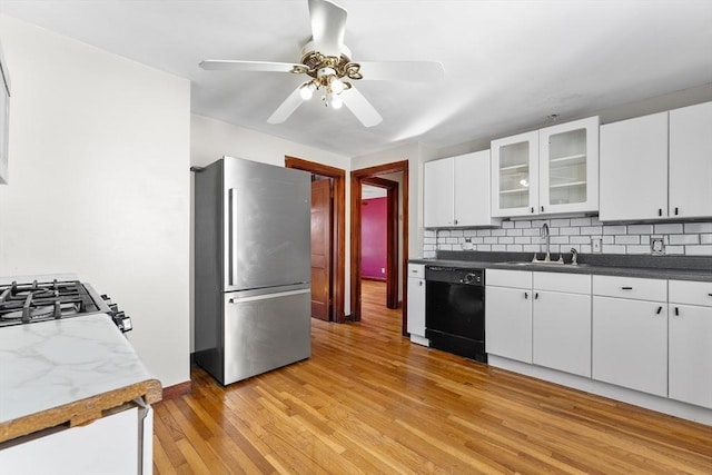 kitchen with glass insert cabinets, freestanding refrigerator, white cabinetry, a sink, and dishwasher